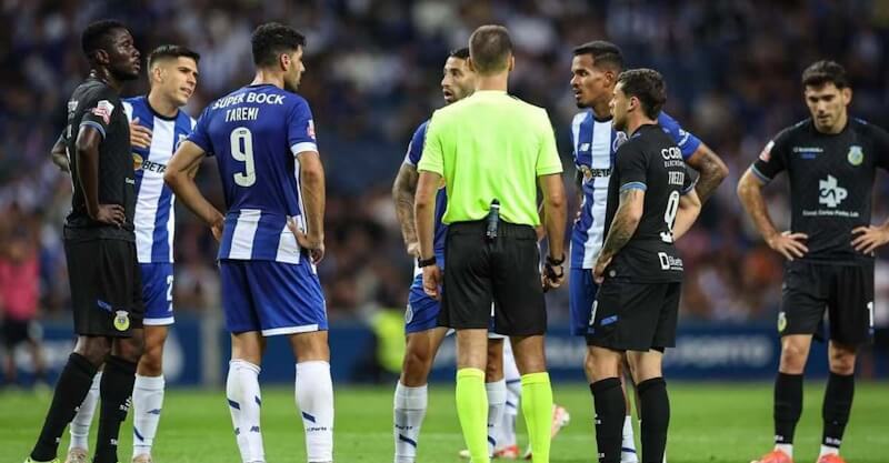 Jogadores de FC Porto e Arouca rodeiam o árbitro Miguel Nogueira.